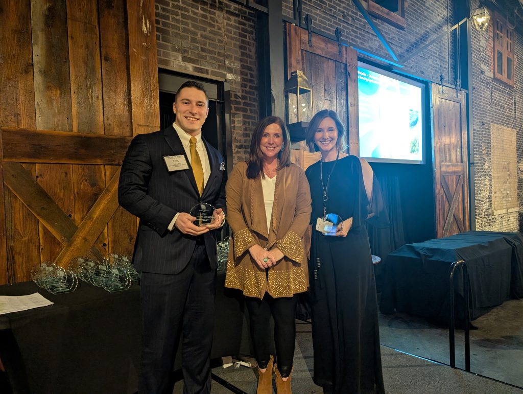 3 people standing with award on stage