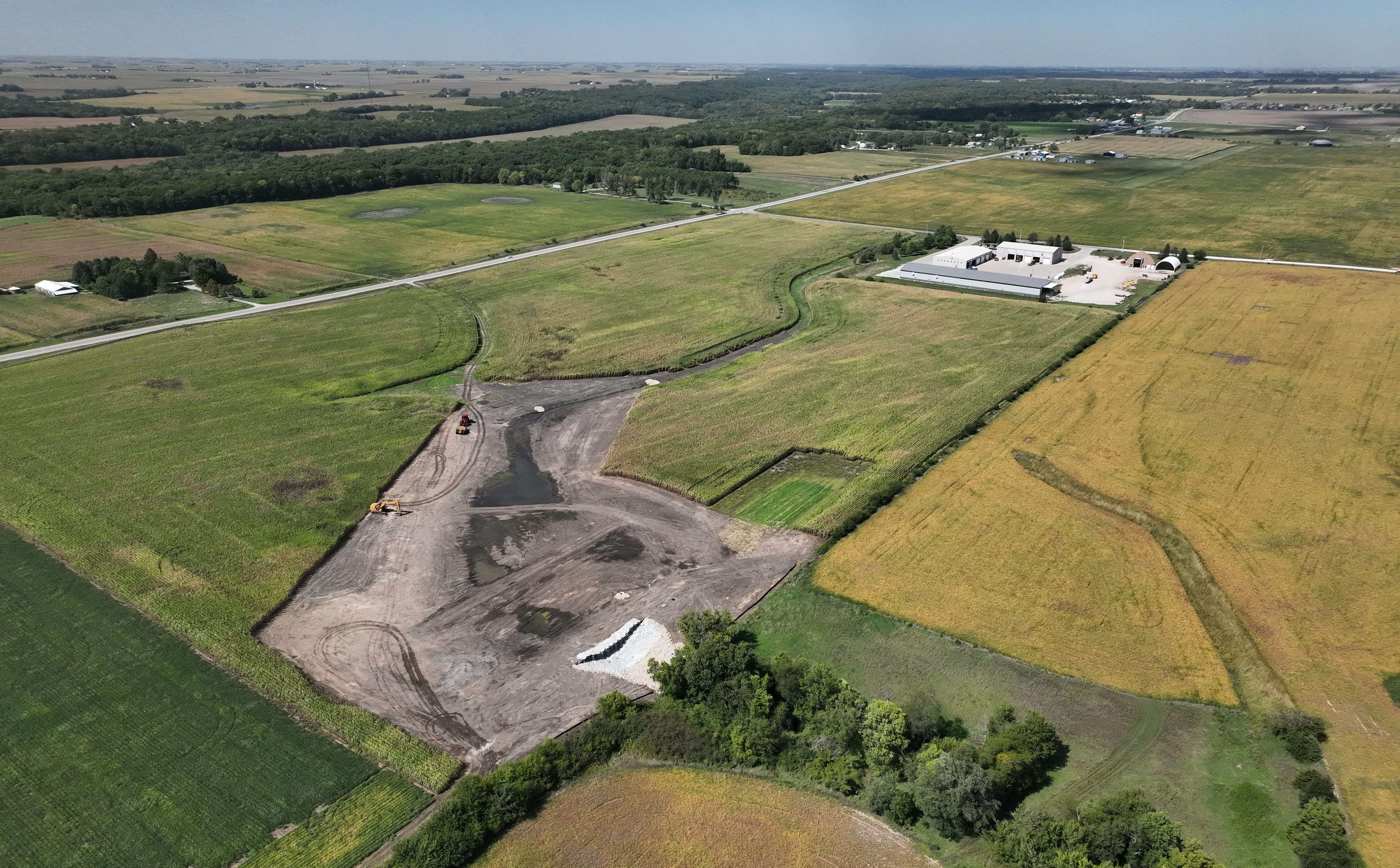 A wetland construction site is seen in aerial view. The cleared-out site is surrounded by farmland.
