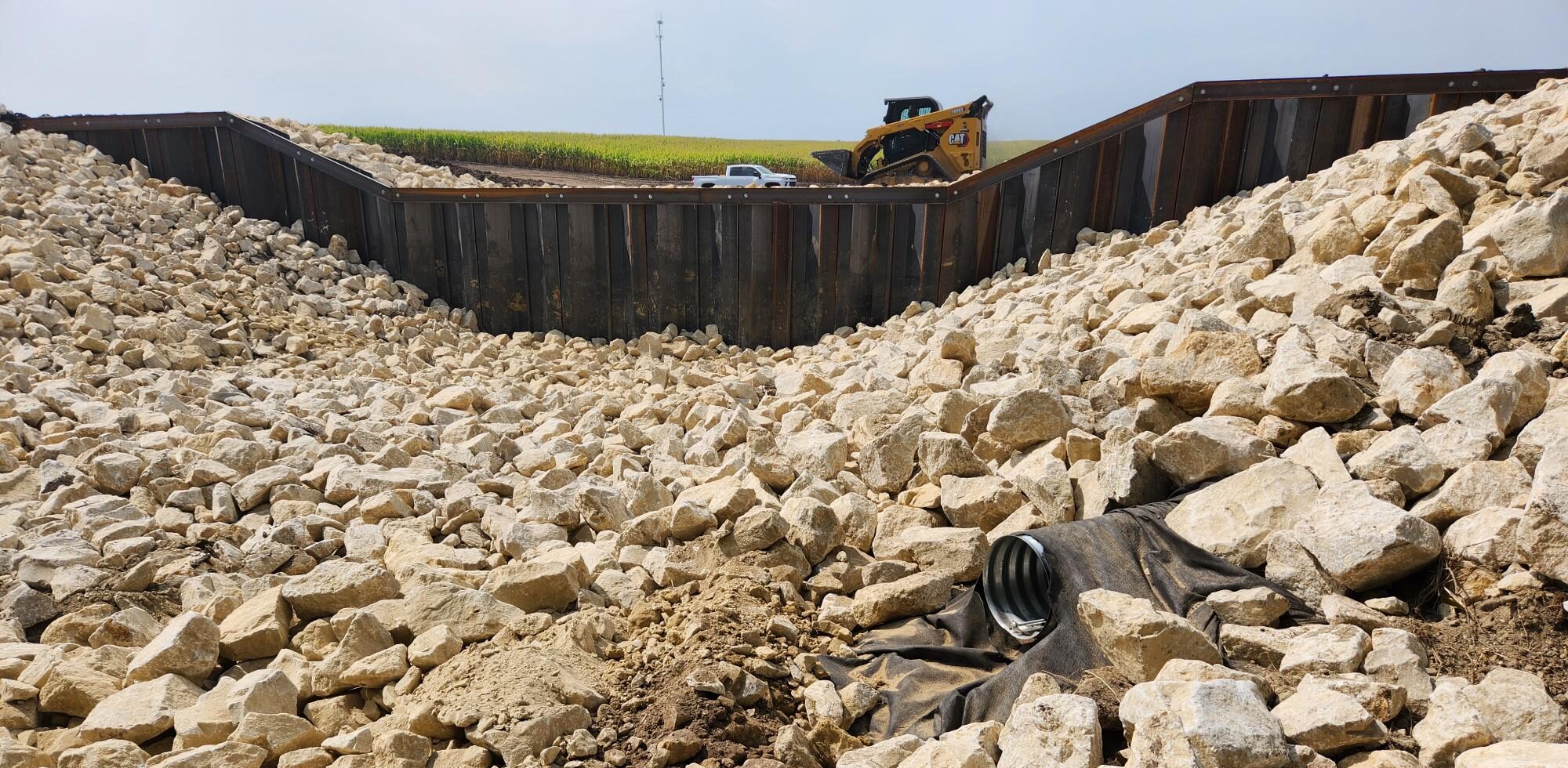 A wetland spillway and drain pipe is seen surrounded by large rocks.