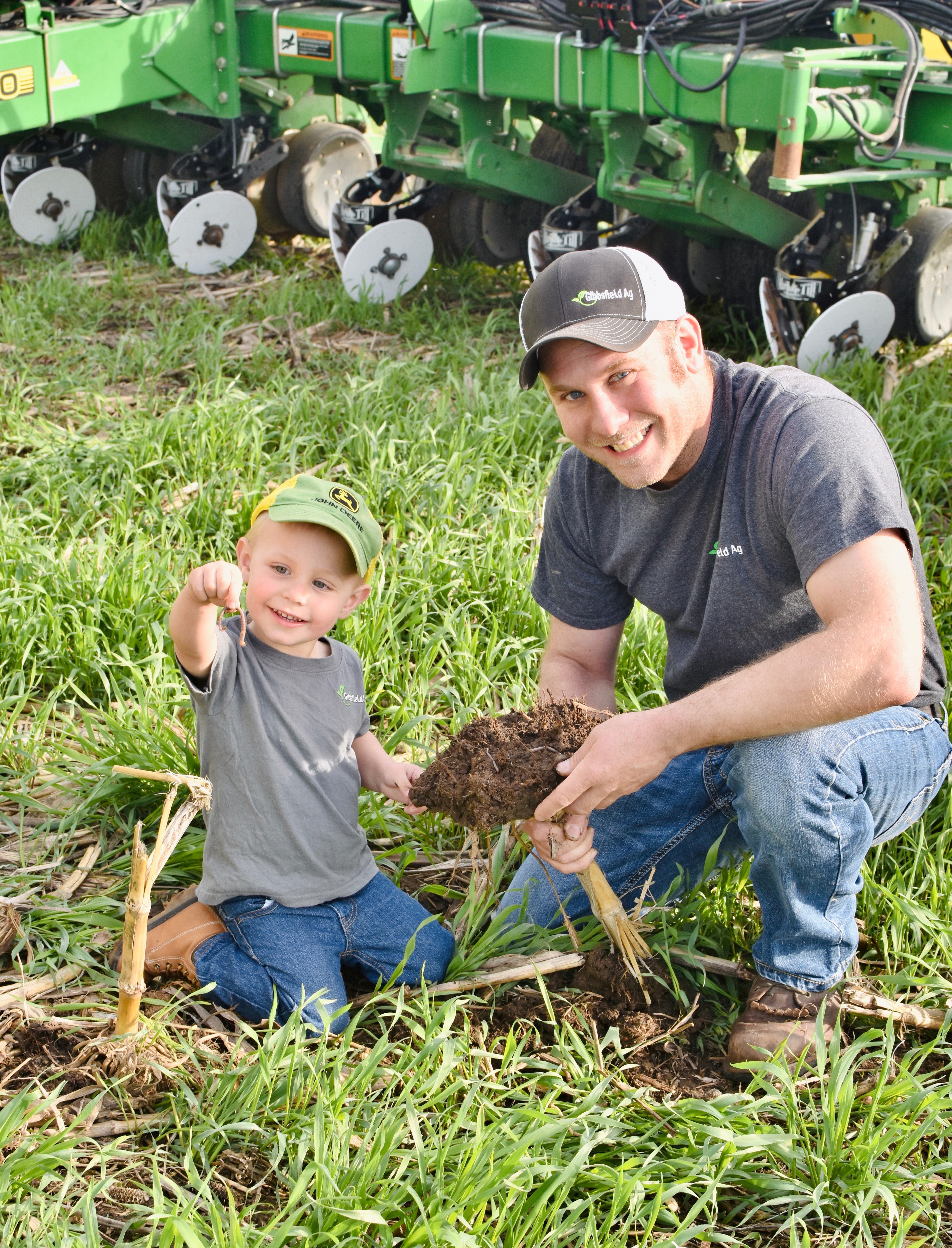 Kendrick poses with a worm next to his dad in a field of cover crops