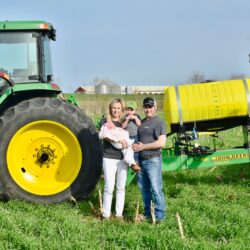 Family standing in front of a tractor in a field