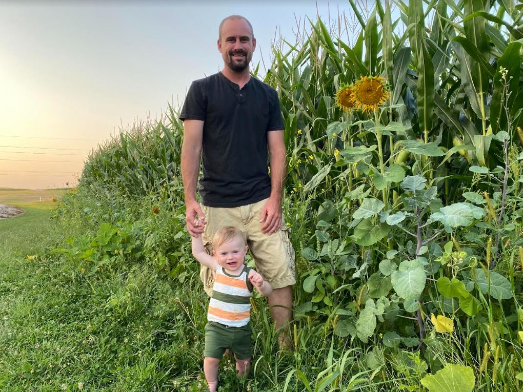 Miller standing next to corn with toddler son