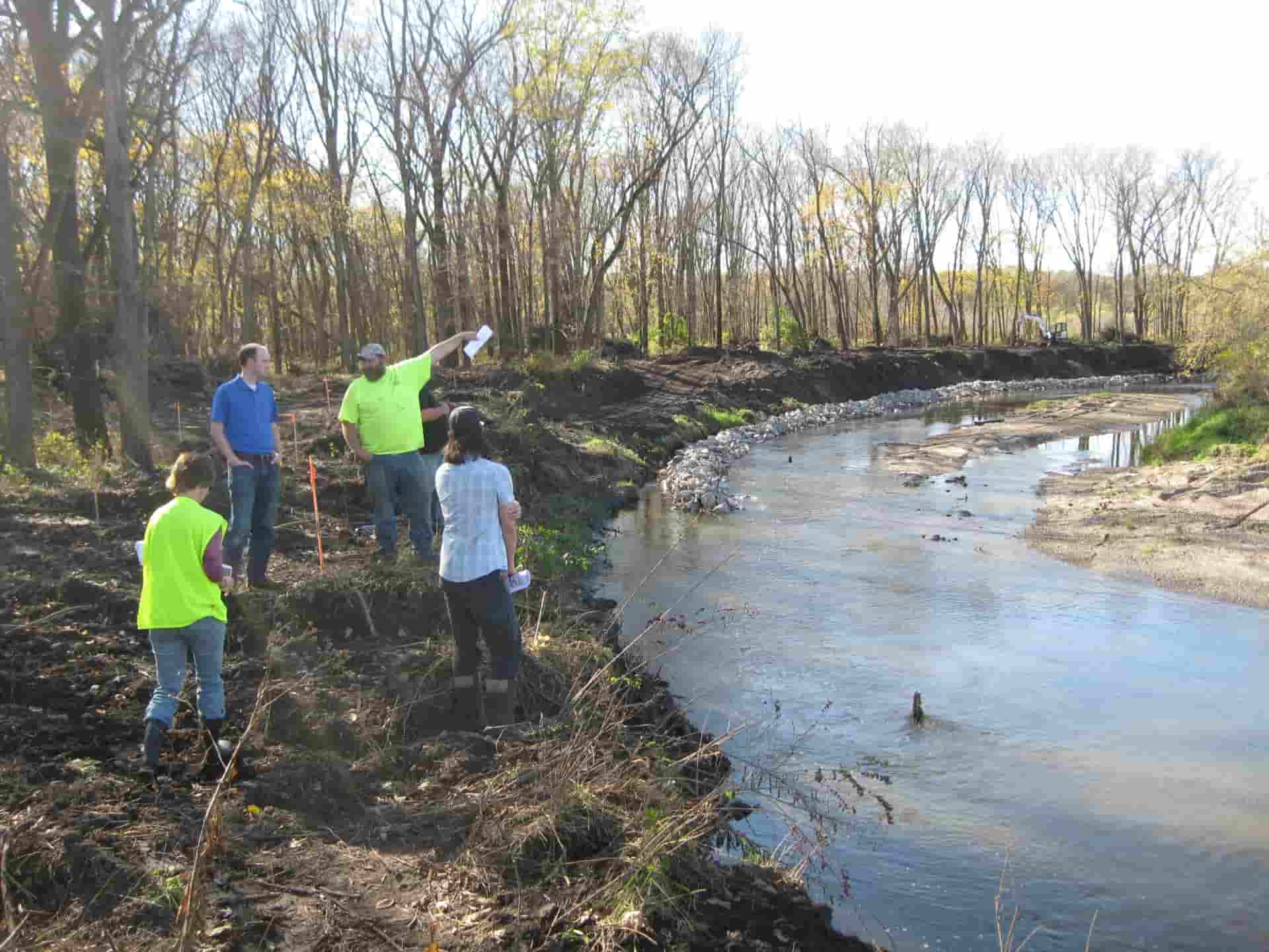 Four people standing over the waterway that is mid-construction