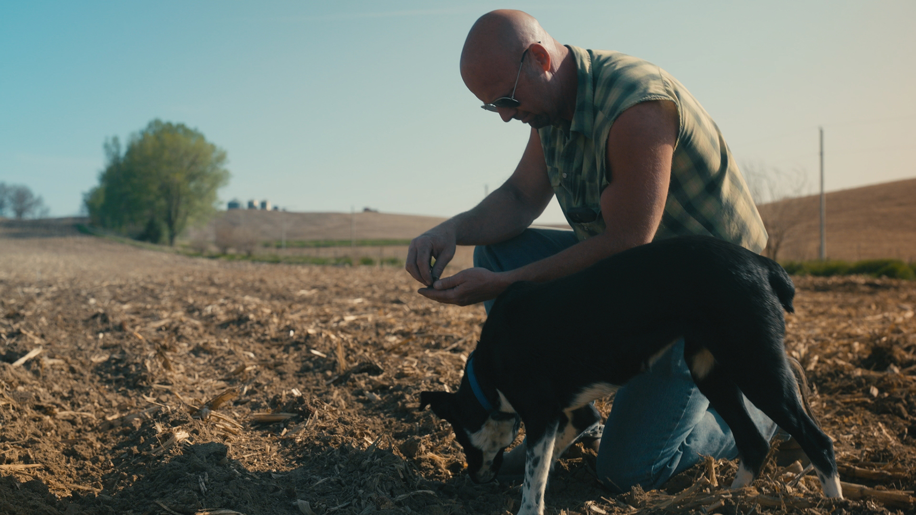 Iowa regenerative farmer Kelly Garrett kneels in a crop field, looking at a handful of soil.