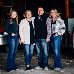 Kerri Bell and her family - a husband and two daughters - smile for a family photo in the entrance of a farm storage shed.