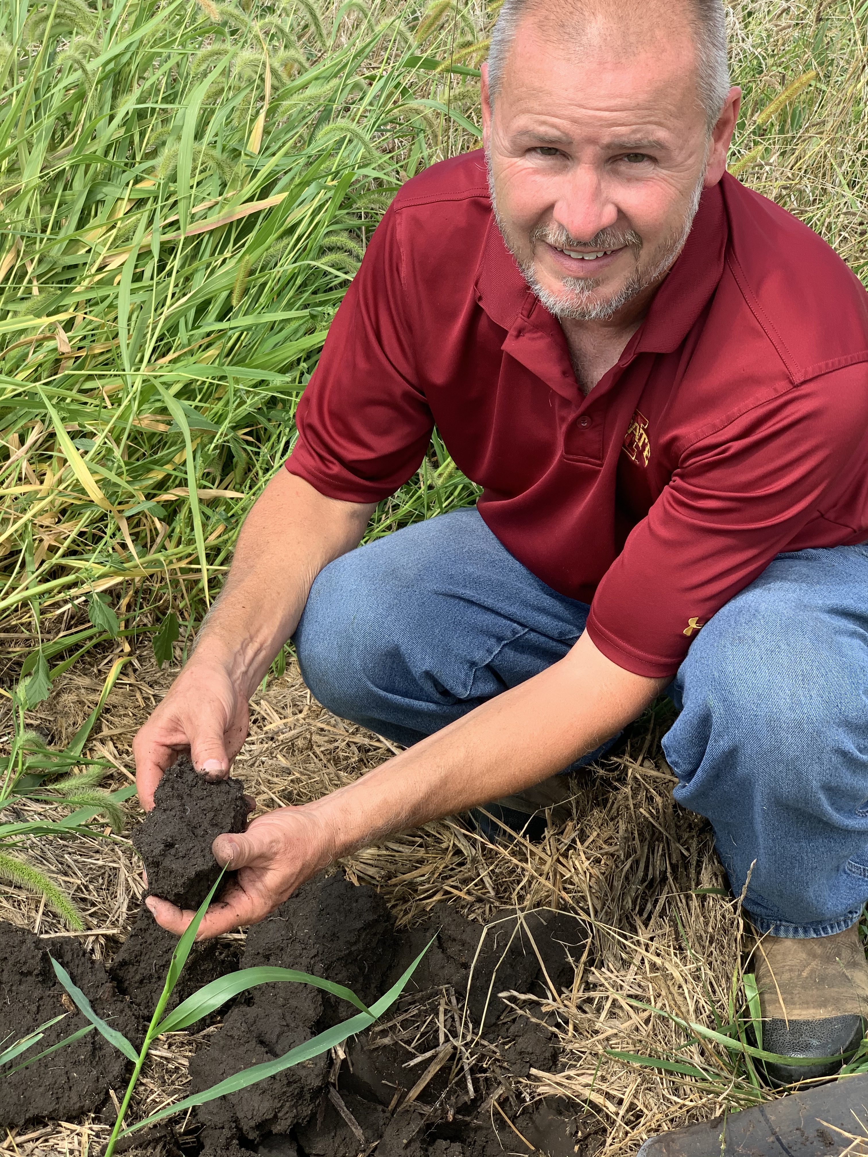 Bretz kneels in field and holds handful of soil